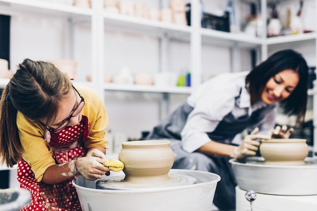 Happy mother and daughter making clay pottery on a spin wheel.