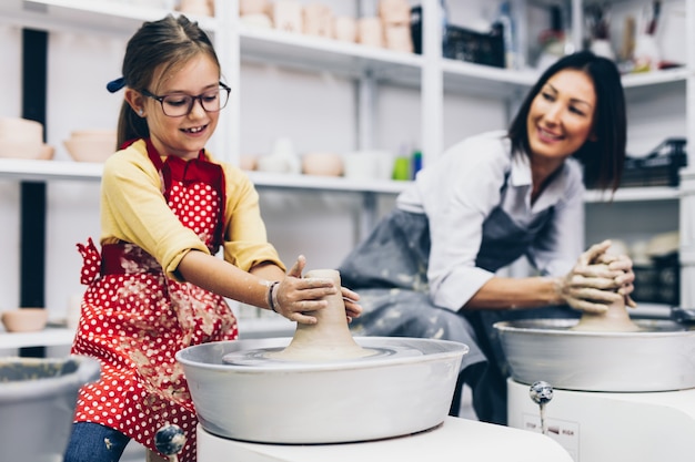 Happy mother and daughter making clay pottery on a spin wheel.