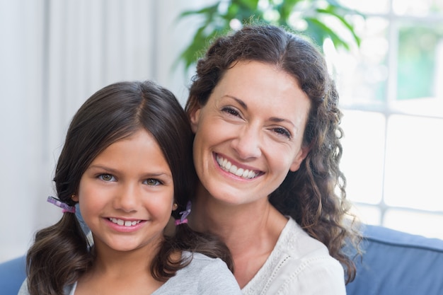 Happy mother and daughter sitting on the couch and smiling at camera 