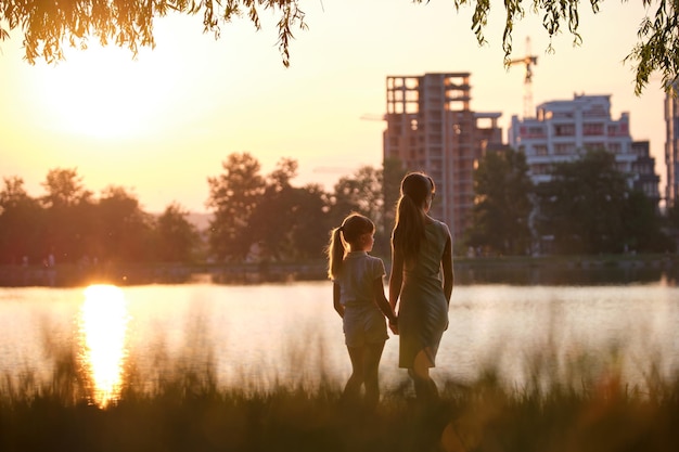 Happy mother and daughter standing together looking at building under construction dreaming about their future home at sunset Family love and relationship concept