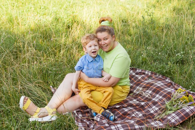 A happy mother and a disabled child are sitting on the grass in the park and gently hugging. Summer holidays. Disability.