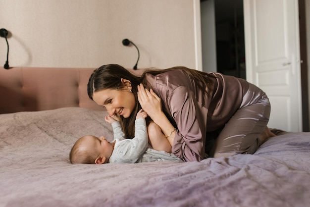 Happy mother having fun and laughing with her baby on the bed