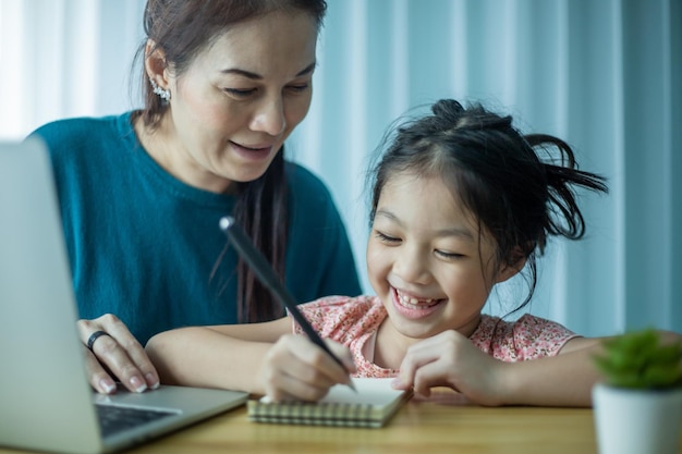 Happy mother helping her cute daughter study online at home Parent and child watching art lesson together on laptop