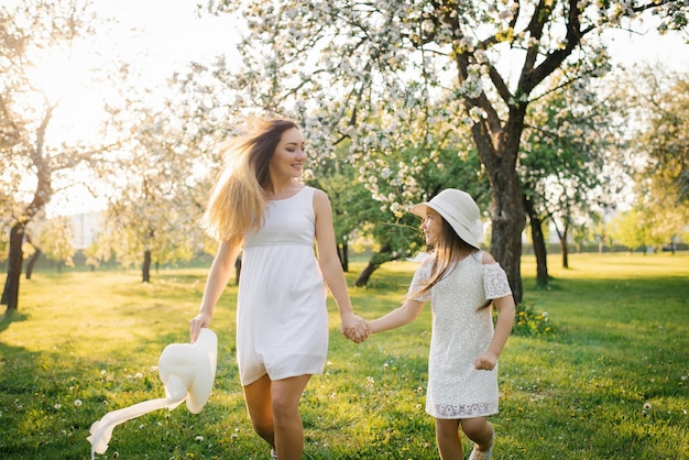 Happy mother and her daughter in white dresses run through the spring garden at sunset