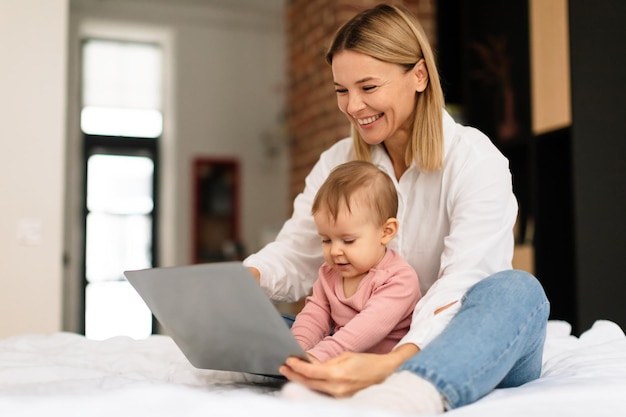 Happy mother and her little daughter using laptop computer at home woman showing cartoons to toddler child