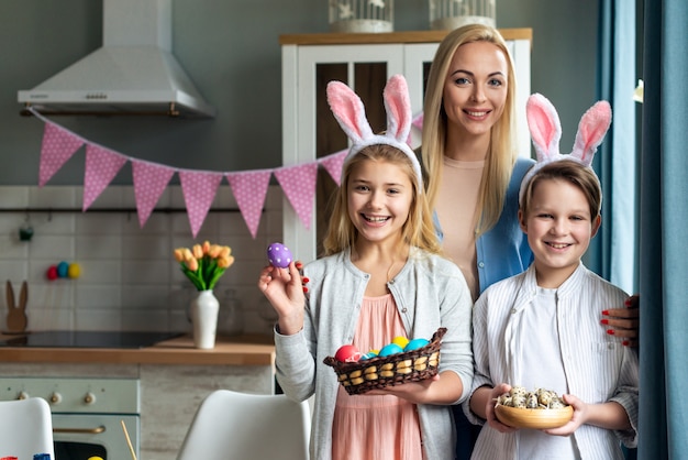 Happy mother and her smiling, lovely children holding colorful eggs and genuinely happy Easter