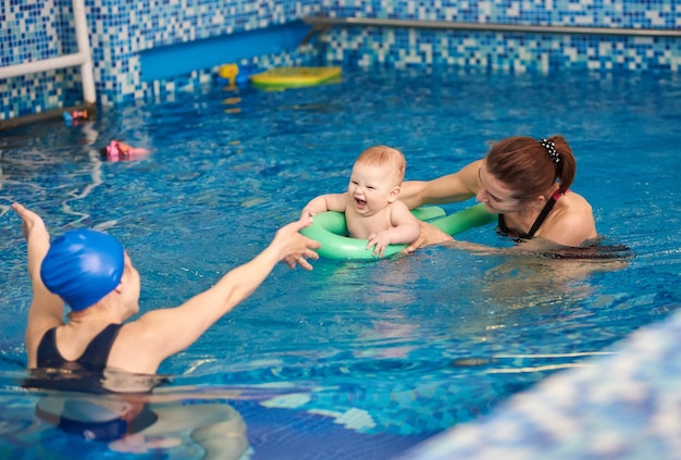 Happy mother and her son laughing baby boy having fun during swimming exercising with trainer in paddling swimming pool