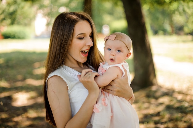 Happy mother holding her little emotional daughter on hands in the park