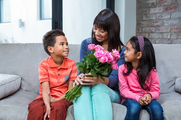 Happy mother holding roses sitting with her son and daughter on the sofa