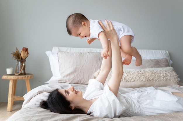 Happy mother holds baby in the air A young mother is playing on the bed with her child Happy childhood