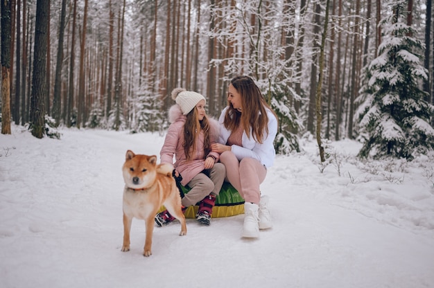 Happy mother and little cute girl in pink warm outwear walking having fun rides inflatable snow tube