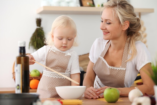 Happy mother and little daughter cooking in kitchen. Spending time all together, family fun concept.