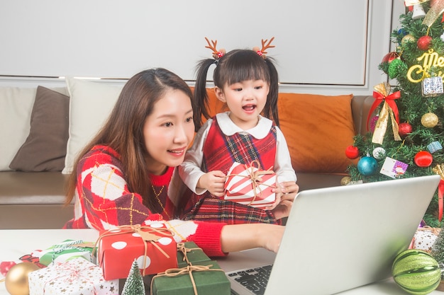 Happy mother and little daughter decorating Christmas tree and gifts at home