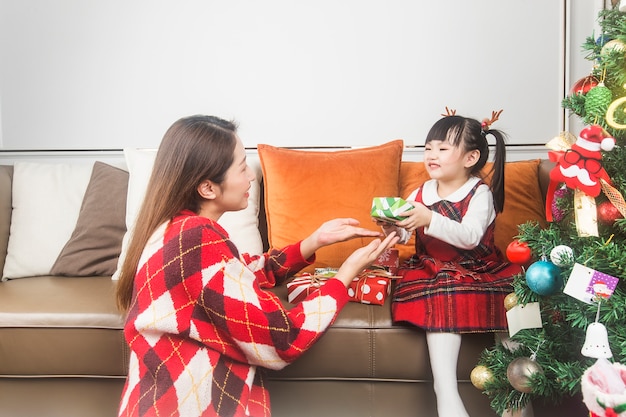 Happy mother and little daughter decorating Christmas tree and gifts at home