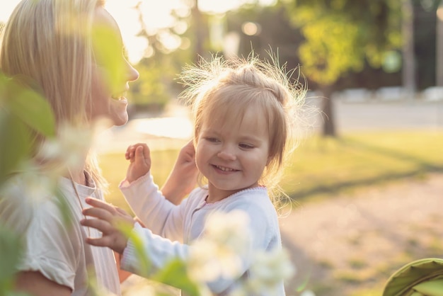 Happy mother and little daughter in the park on a sunny day at sunset Mom and child outdoor Concept of tenderness family single mother flowers smiles hugs mental health harmony