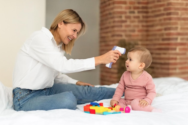 Happy mother measuring temperature of her little daughter child with noncontact infrared thermomete