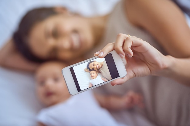 Photo happy mother phone screen and selfie with baby on bed for memory picture or photography at home hand of mom with smile little infant or child in bedroom motherhood moment or capture at house