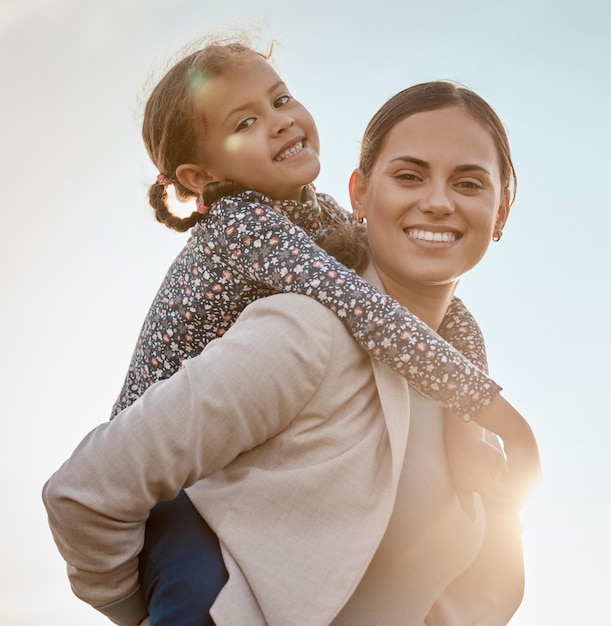 Photo happy mother portrait and piggyback with child for fun bonding holiday or weekend together in nature mom carying daughter little girl or kid on back with blue sky or sunrise for outdoor walk