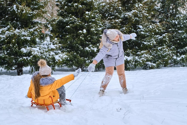 Happy mother pulling sledge with kid girl on snowy park road