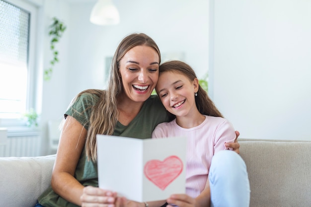 Happy mother's day! Child daughter congratulates mom and gives her postcard. Mum and girl smiling and hugging. Family holiday and togetherness.