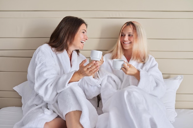 Happy mother and teenage daughter drinking coffee and talking