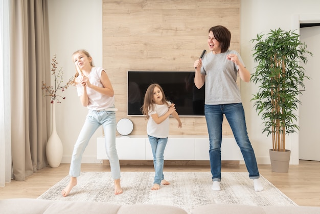 Happy mother and two daughters having fun singing karaoke song in hairbrushes. mother laughing enjoying funny lifestyle activity with teenage girl at home together.