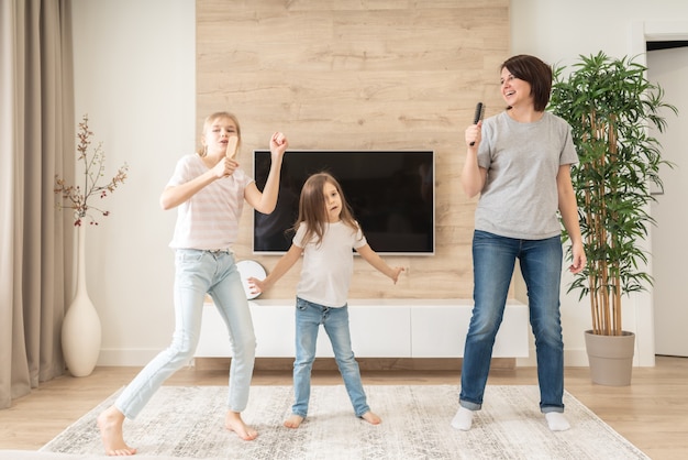 Happy mother and two daughters having fun singing karaoke song in hairbrushes.