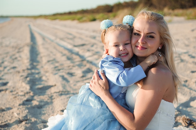 Happy mother in the wedding dress with her daughter on the beach.