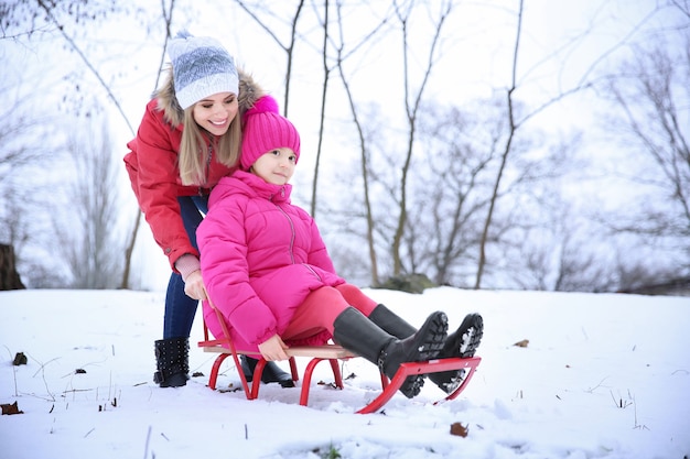 Happy mother with daughter sledding in snowy park on winter vacation