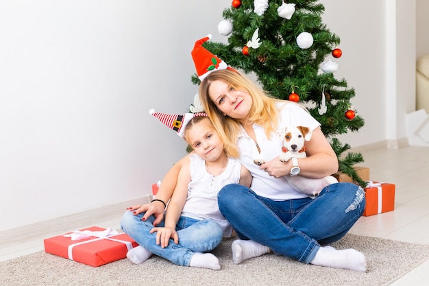 Happy mother with her daughter and jack russell terrier dog sitting near the Christmas tree