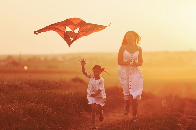 Happy mother with her little daughter have fun by playing with kite outdoors on the field