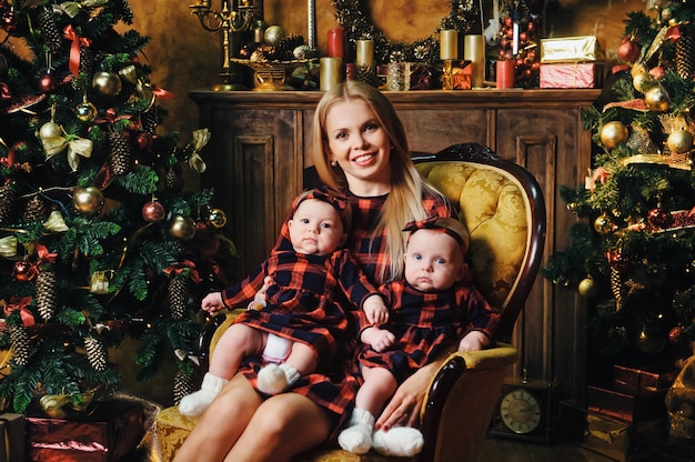 A happy mother with her twin children in the New Year's interior of the house on the background of a Christmas tree