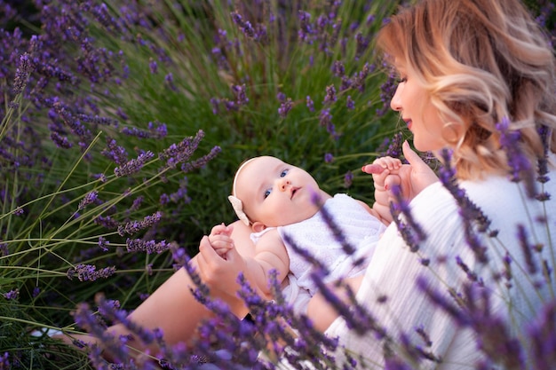 Happy mother with pretty daughter on lavender background. Beautiful woman and cute baby sitting in m