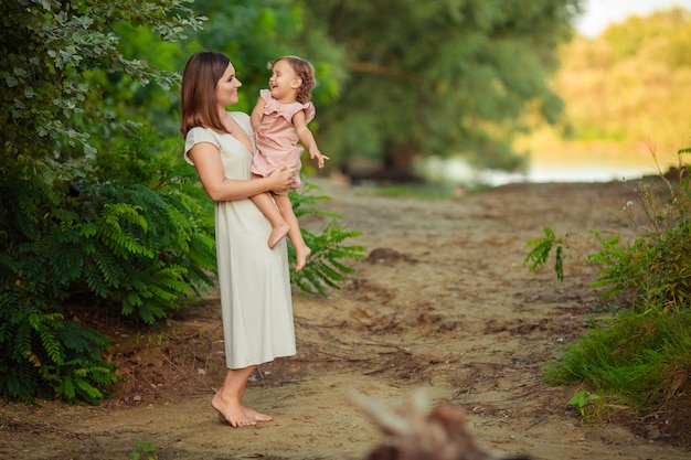 happy motherhood. mother and daughter have fun on a walk on vacation on the sandy bank of the river in summer