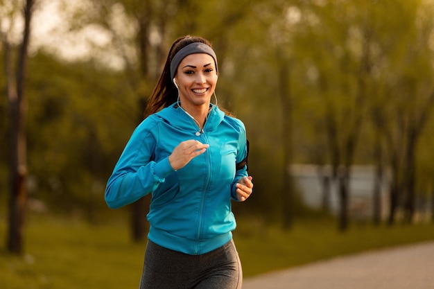 Happy motivated sportswoman running in the park and looking at camera