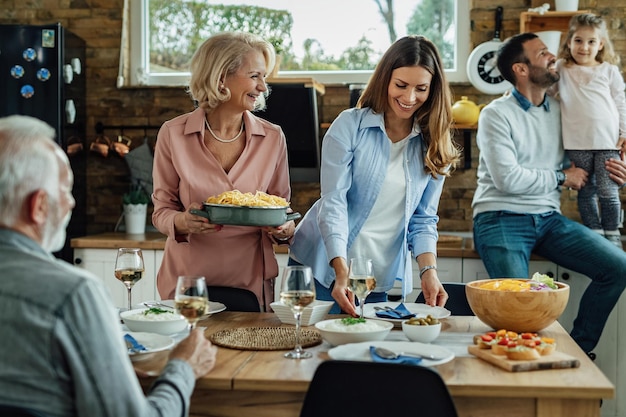 Happy multi-generation family having lunch together in dining room. Focus is on women brining food at the table.