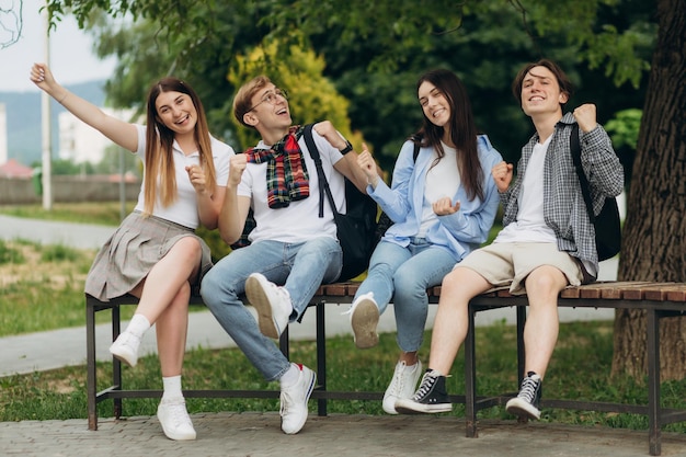 Happy multiethnic friends sitting in park and showing rejoice gesture