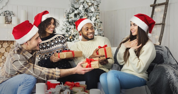 Happy multiracial friends sharing presents near nicely decorated christmas tree