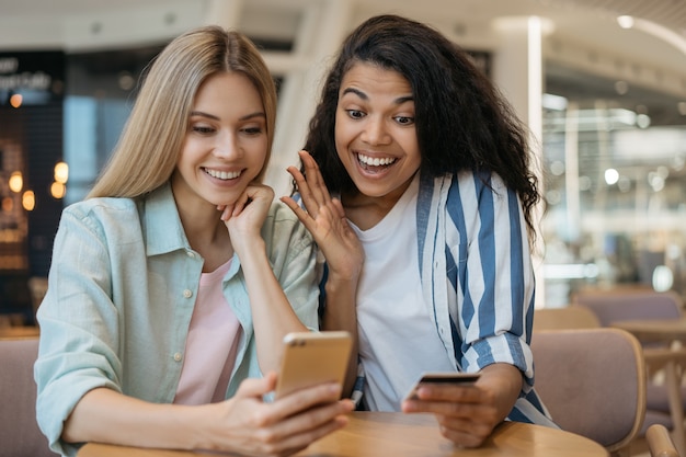 Happy multiracial friends shopping online with big sales, sitting together at table