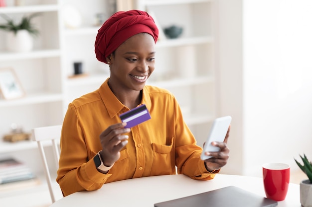 Happy muslim african american woman using smartphone and credit card