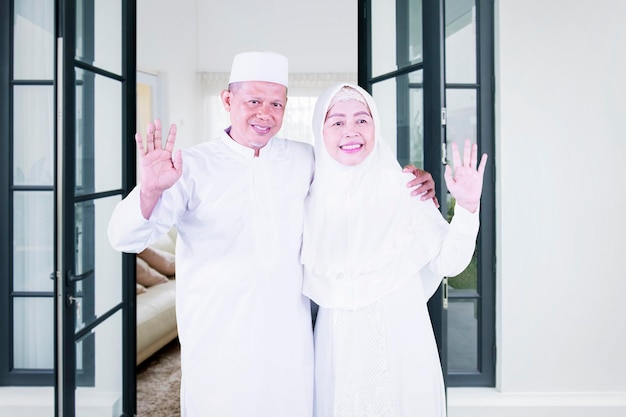 Happy Muslim couple waving hands together at home