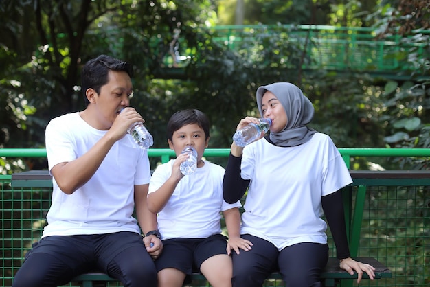 Happy Muslim family holding bottle with water and drinking while resting after sport workout outdoor