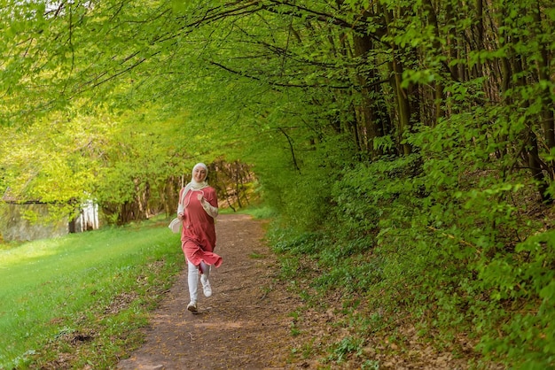 Happy muslim sports fit woman in hijab trail running outdoor in the summer park