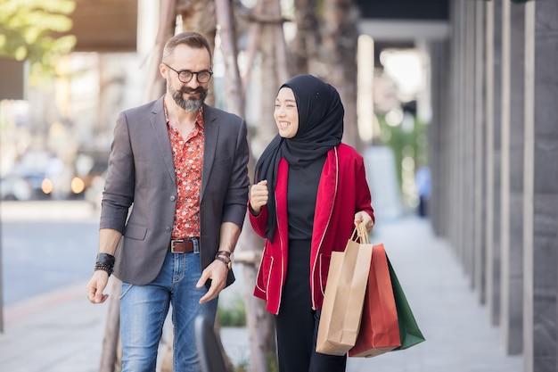 Happy muslim woman and boy freind with city shopping hand holding paper bags