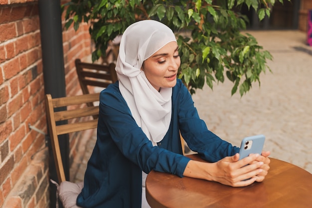 Happy muslim woman having video call on smartphone in city.