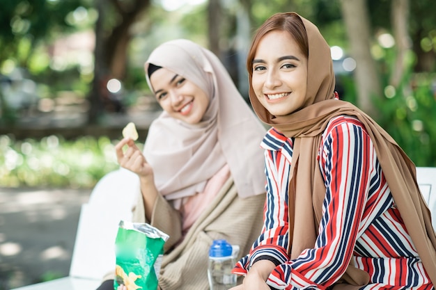 Happy muslim young woman with friend enjoy their snack while relaxing in the park