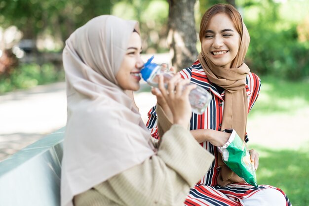 Happy muslim young woman with friend enjoy their snack while relaxing in the park