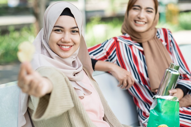 Happy muslim young woman with friend enjoy their snack while relaxing in the park