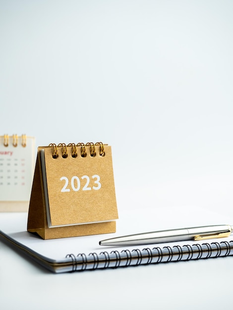 Happy new year 2023 background 2023 numbers year on small beige desk calendar cover on notepad with pen on white background with copy space vertical style