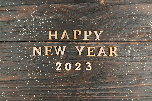 Happy New year 2023 celebration Wooden text on wooden background with scattered golden confetti Flat lay